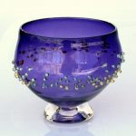 A purple glass bowl with gold and silver beads.