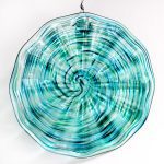 A blue and green glass dish hanging on the wall.